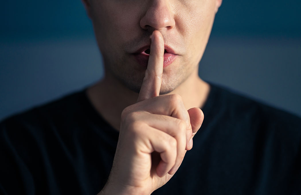 Eine Person signalisiert mit dem Zeigfinger am Mund Ruhe.