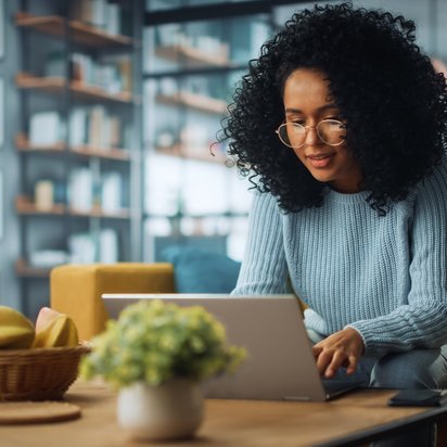 Eine Frau arbeitet am Couchtisch an ihrem Laptop.