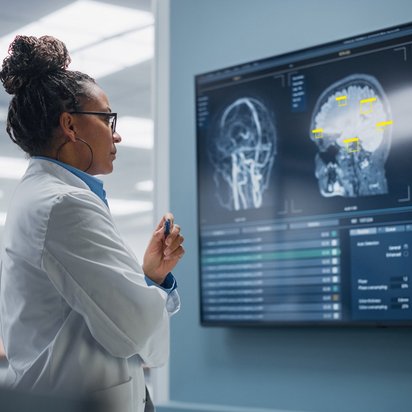 Eine Medizinerin steht vor einem Bildschirm, auf dem bildgebende KI einen medizinischen Scan auswertet. 