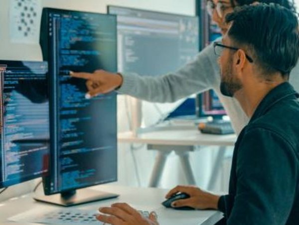 Eine Mitarbeitende zeigt einem Kollegen etwas im Code auf dem Bildschirm