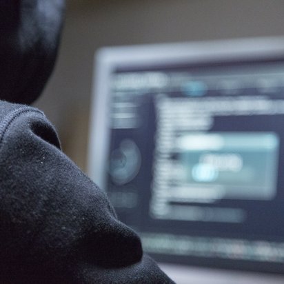 code-daten-hacking Eine Person mit Kapuzenpulli sitzt an einem Monitor mit Code.