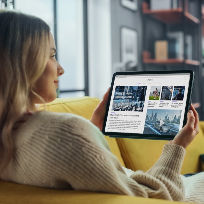 Eine Frau sitzt auf einem Sofa und ließt Online Artikel auf ihrem Tablett