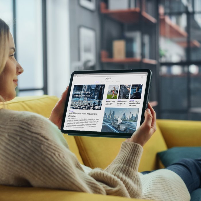 Eine Frau sitzt auf einem Sofa und ließt Online Artikel auf ihrem Tablett