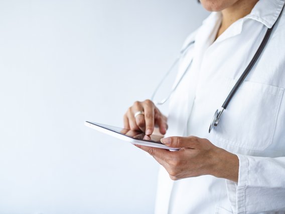 Ein Arzt oder eine Ärztin hält ein Tablet in der Hand.