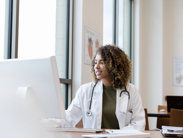 A doctor sits at her desk and works on her computer.