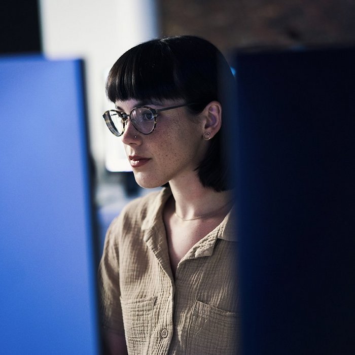 Eine junge Frau blickt auf zwei Bildschirme und arbeitet in einem digitalen Workflow