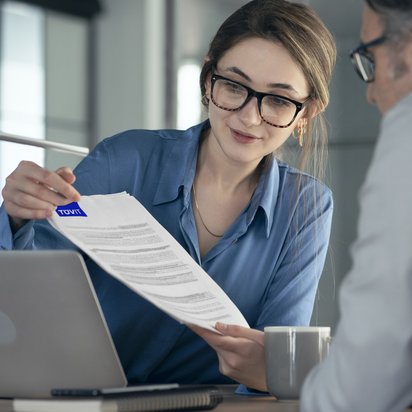 Eine Frau zeigt einem Mann etwas auf einem Dokument, auf dem Textpassagen markiert sind.