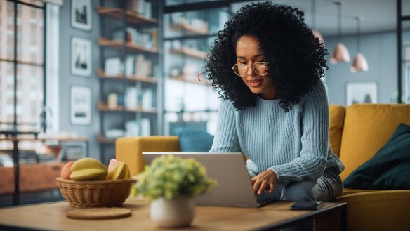 Eine Frau arbeitet am Couchtisch an ihrem Laptop. | TÜVIT