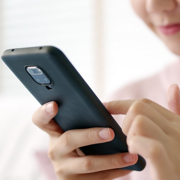 Eine Frau bedient lächelnd ihr Smartphone. | TÜVIT