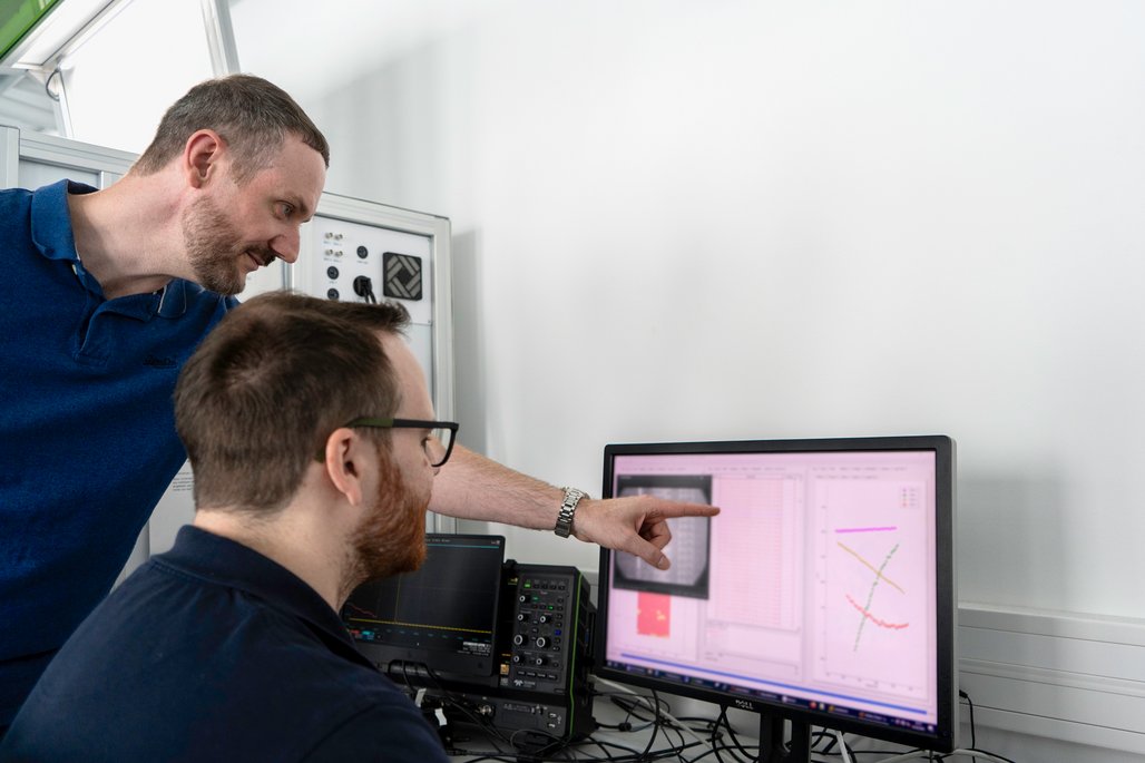 Mitarbeitende im TÜVIT Hardware-Labor werten Prüfergebnisse am Monitor aus