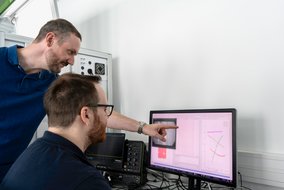 Mitarbeitende im TÜVIT Hardware-Labor werten Prüfergebnisse am Monitor aus