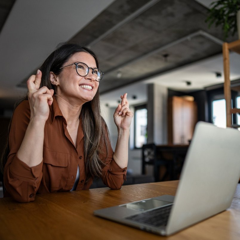 A woman crosses her fingers, hoping for luck in a contest on her laptop