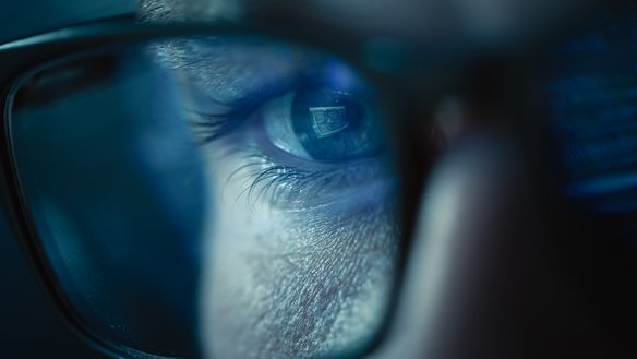 Nahaufnahme eines Brillenglases einer Person, die auf einem Monitor schaut