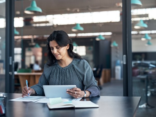 A woman works with a tablet and lists on paper