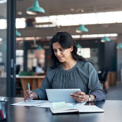 Eine Frau arbeitet an einem Tisch mit einem Tablet und Papier.