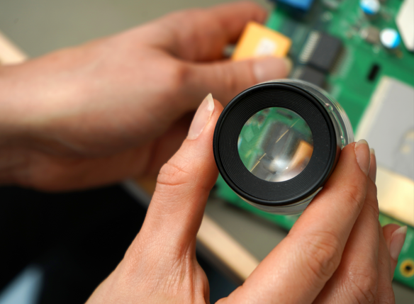 Close-up of a magnifying glass over a PCB board.