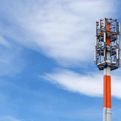 Mobilfunkmast in Rot und Weiß vor blauem Himmel.