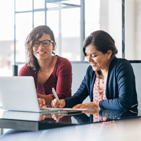Zwei Frauen am Schreibtisch. Zwei Frauen arbeiten an einem Schreibtisch mit einem Laptop vor ihnen.