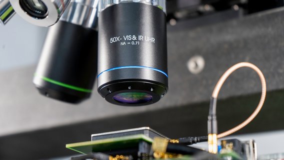 hardware-labor-laser-faultinjection-objektivlinse Lasergestützte Faultinjection (LFI) eines Samsung Mobile Chips. Die Objektivlinse der Laseroptik fokussiert den Laserstrahl direkt auf die Schaltstrukturen des Chips.