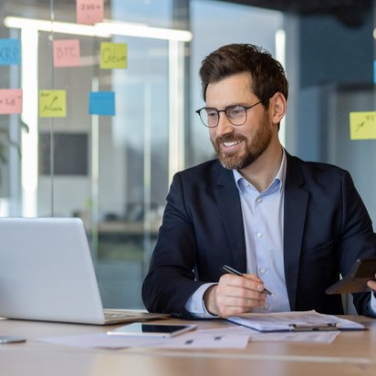 Ein Mann sitzt in einem Büro an einem Laptop und lächelt.