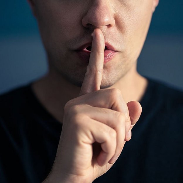 Eine Person signalisiert mit dem Zeigfinger am Mund Ruhe.