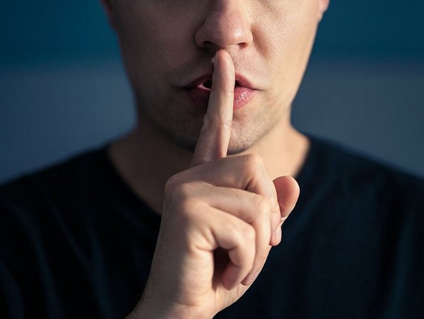 Eine Person signalisiert mit dem Zeigfinger am Mund Ruhe.