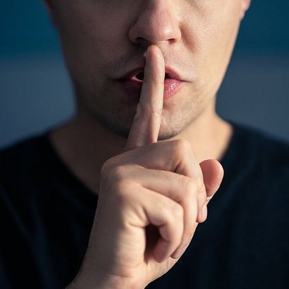 Eine Person signalisiert mit dem Zeigfinger am Mund Ruhe.