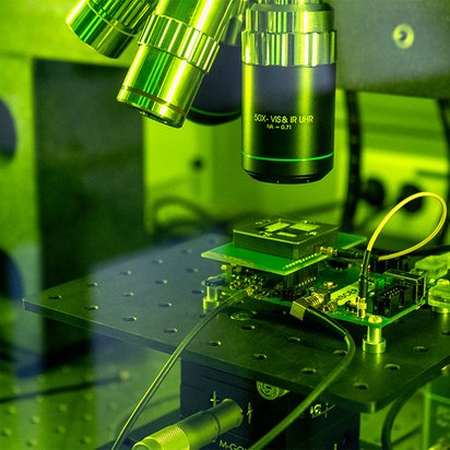 laseraufbau-hardwarelabor Das Bild zeigt einen Laseraufbau im TÜVIT-Hardwarelabor hinter einer grünen Glaswand