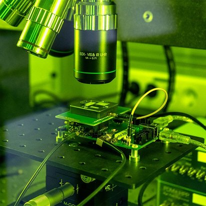 Das Bild zeigt einen Laseraufbau im TÜVIT-Hardwarelabor hinter einer grünen Glaswand